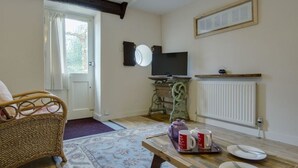 Una habitación acogedora con una silla de mimbre, una mesa de comedor con platos y una tetera, un televisor y un radiador.
