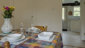 Una mesa de comedor dispuesta con platos, cuencos y vasos blancos, un florero con flores y un mantel colorido.