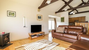 A living room with a wooden ceiling, a television on a wooden stand, a brown leather sofa, and a patterned rug.