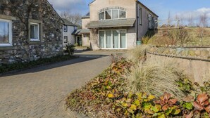 A stone house with a paved driveway and a garden with various plants.