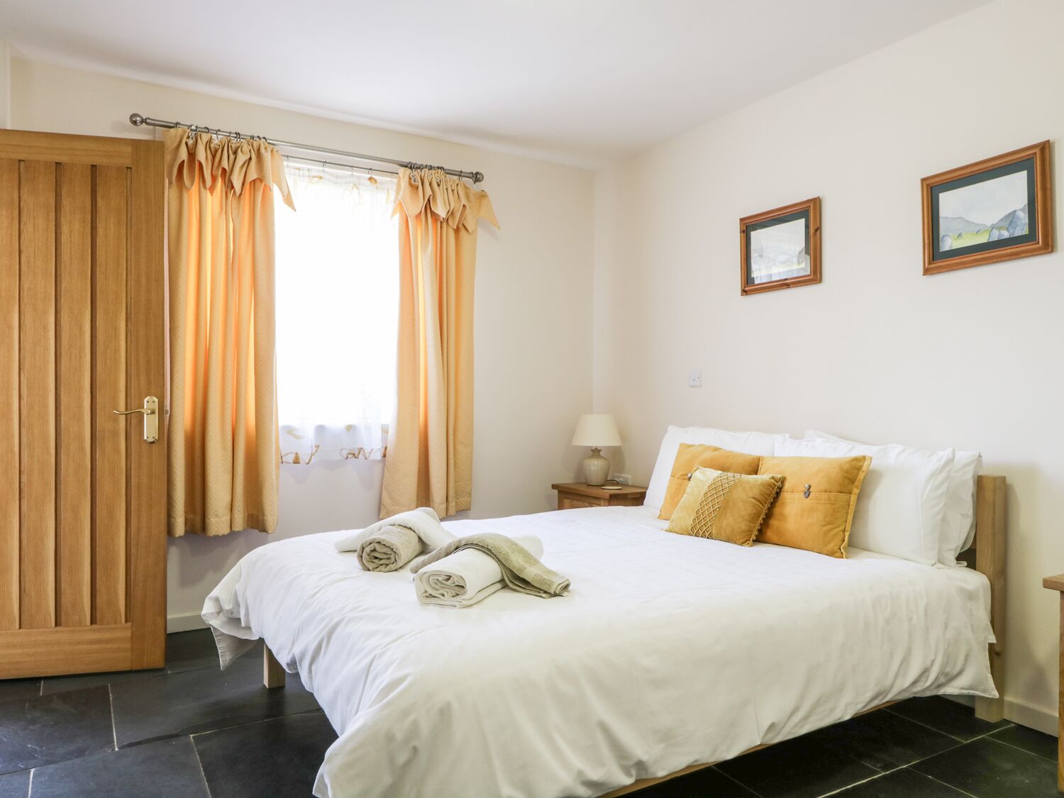 Quarto com cama, cortinas, mesa de cabeceira e duas fotos emolduradas na parede.