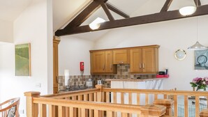 A modern kitchen with wooden cabinets, a built-in oven, and a wooden railing overlooking the dining area.