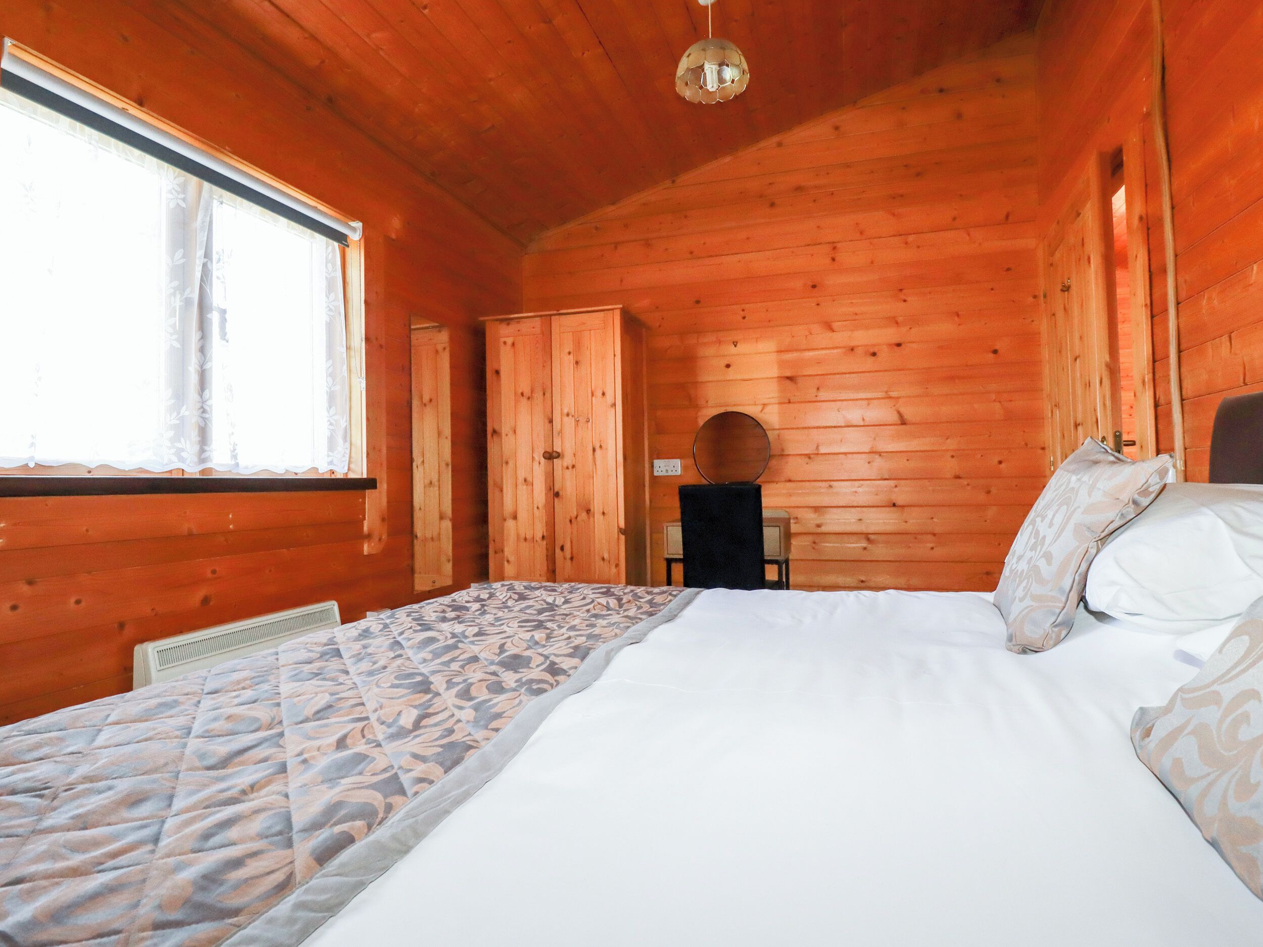 A wooden cabin bedroom with a bed, a dresser, and a mirror.