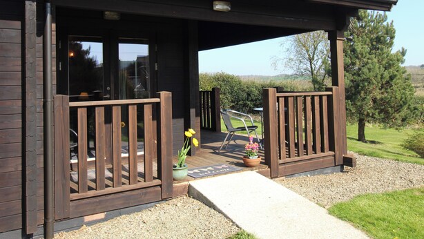 A wooden cabin with a covered porch, a door, and a small garden area with a bench and potted plants.