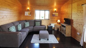 A cozy cabin interior with a sectional sofa, a small ottoman, a television, and a chandelier.