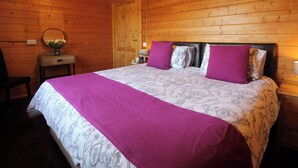 A wooden-paneled bedroom with a bed, a nightstand, a chair, and a mirror.