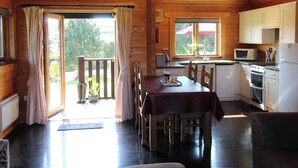 A wooden cabin with a dining area, kitchen, and a balcony with curtains.
