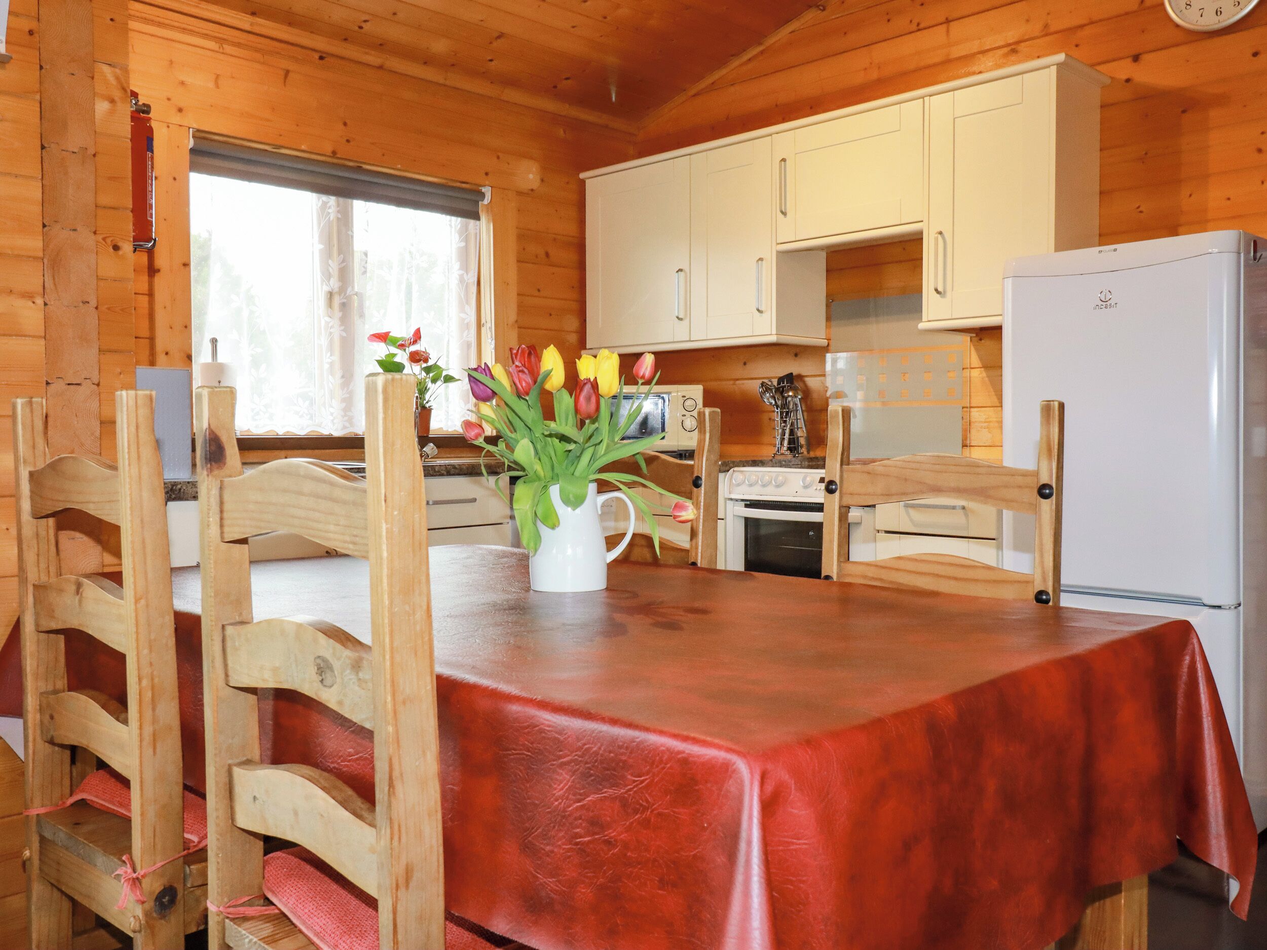 L’intérieur d’un chalet en bois comprend une table à manger, des chaises, un coin cuisine avec un poêle et un réfrigérateur.
