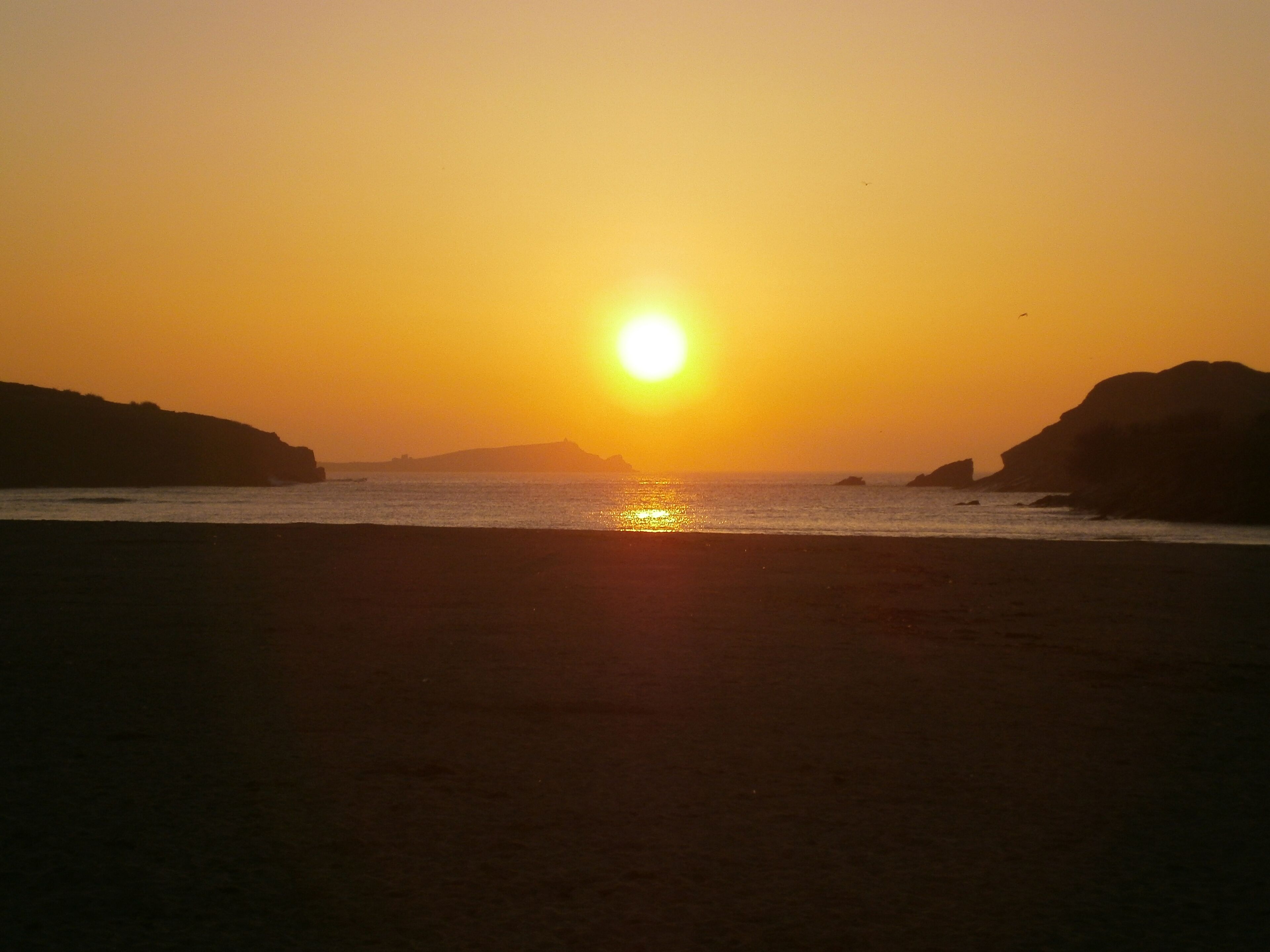 Un coucher de soleil sur une plage, avec les silhouettes de collines en arrière-plan.