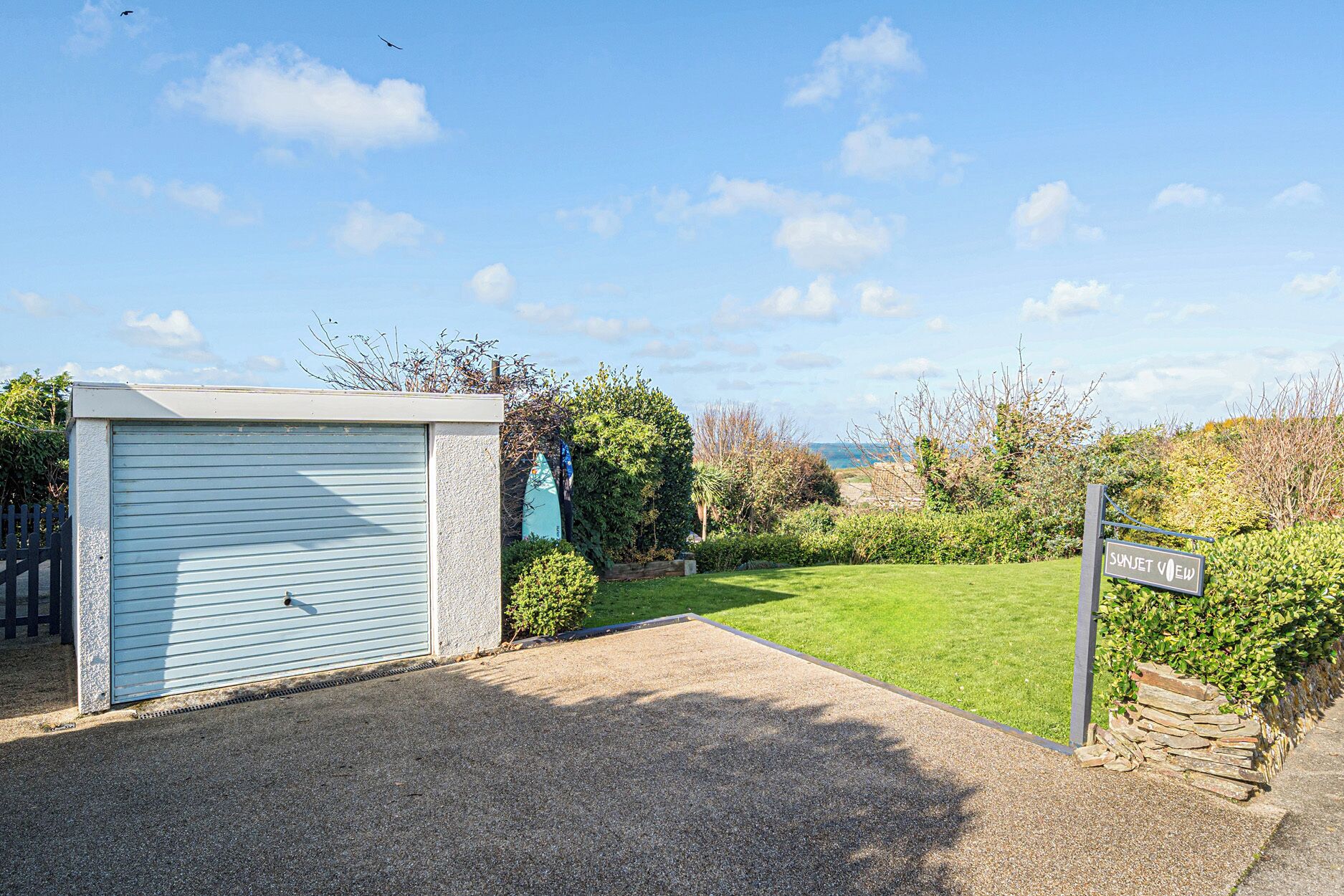 A residential property with a closed garage, a well-maintained lawn, and a sign indicating the property name.