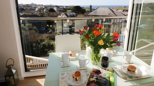 Ein Essbereich mit Tisch für zwei Personen, einer Tulpenvase und einem Buch mit dem Titel „Frühlingsfarben in Falmouth“.