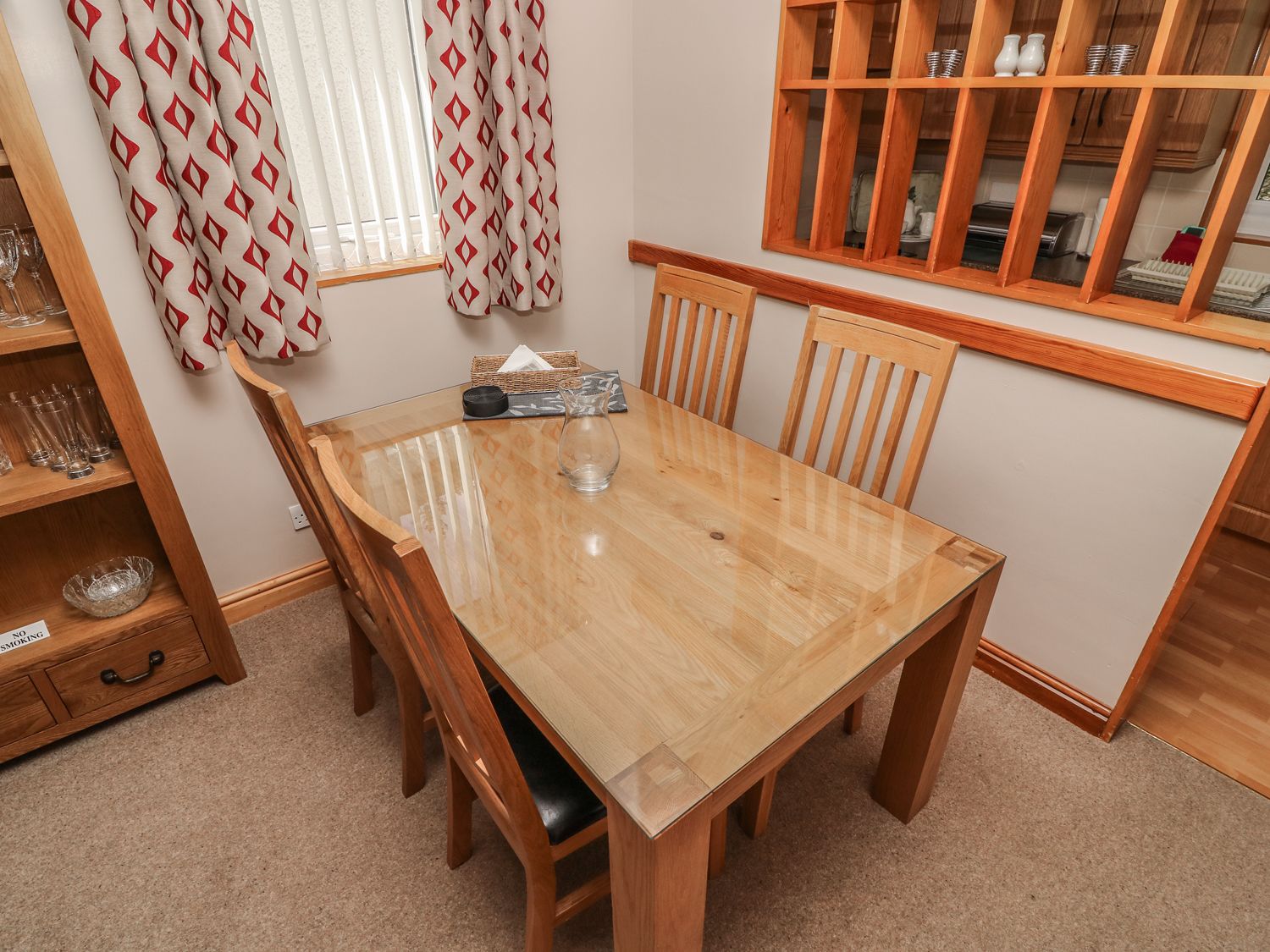 Un coin repas avec une table et des chaises en bois, un vase en verre et une fenêtre avec des rideaux.