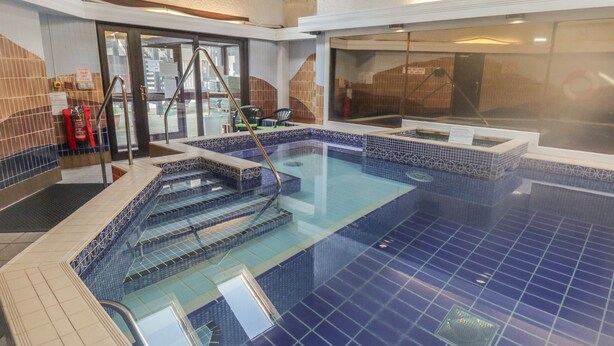 Una piscina con diseño de azulejos azules, una barrera de vidrio y un techo de madera.