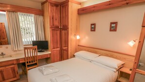 Habitación de hotel con cama, escritorio con computadora, una silla, un espejo y dos luces en la pared.