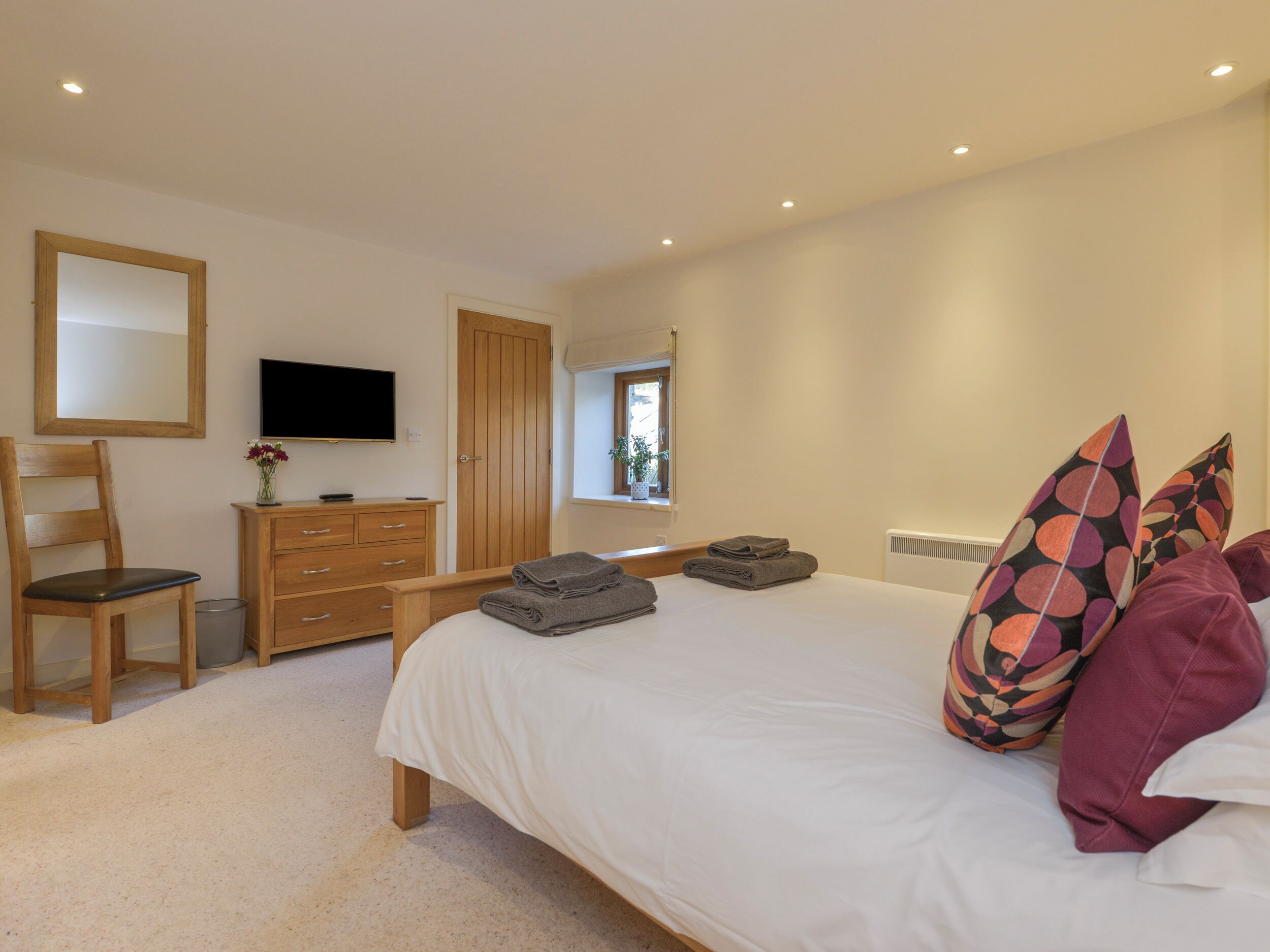 A bedroom with a bed, a wooden dresser, a television, and a window with a view of the outdoors.