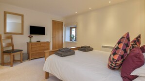 A bedroom with a bed, a wooden dresser, a television, and a window with a view of the outdoors. - Old Armoury Barn (Newton Abbot)