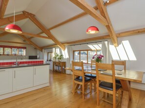 A spacious kitchen with wooden beams, a dining area with a wooden table and chairs, and a large window providing natural light. - Old Armoury Barn (Newton Abbot)