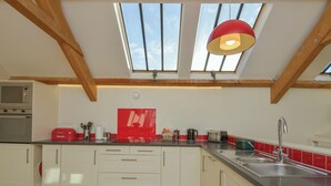 A modern kitchen with skylights, wooden beams, and a red accent wall. - Old Armoury Barn (Newton Abbot)