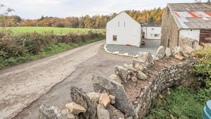 Un camino rural que lleva a un edificio blanco con muro de piedra y un granero de techo rojo.