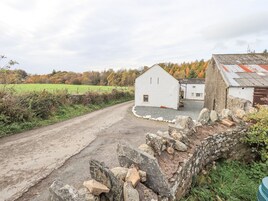 A rural road leading to a white building with a stone wall and a barn with a red roof.