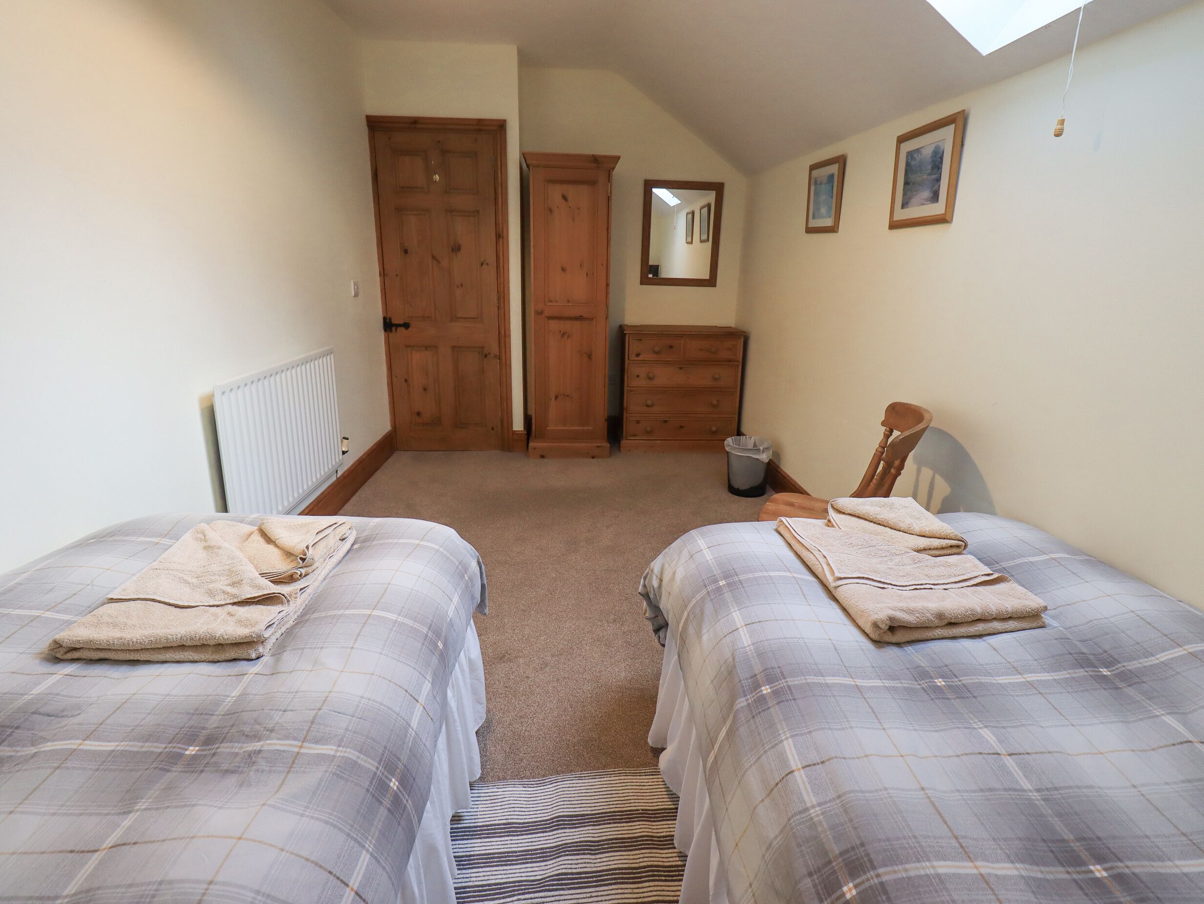 A bedroom with two beds, a wooden dresser, a mirror, and a radiator.