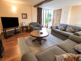A living room with a flat-screen TV, a wooden coffee table, a grey sofa, and a patterned rug.