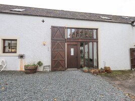 A rustic building with a large wooden door, a window, and a gravel driveway.