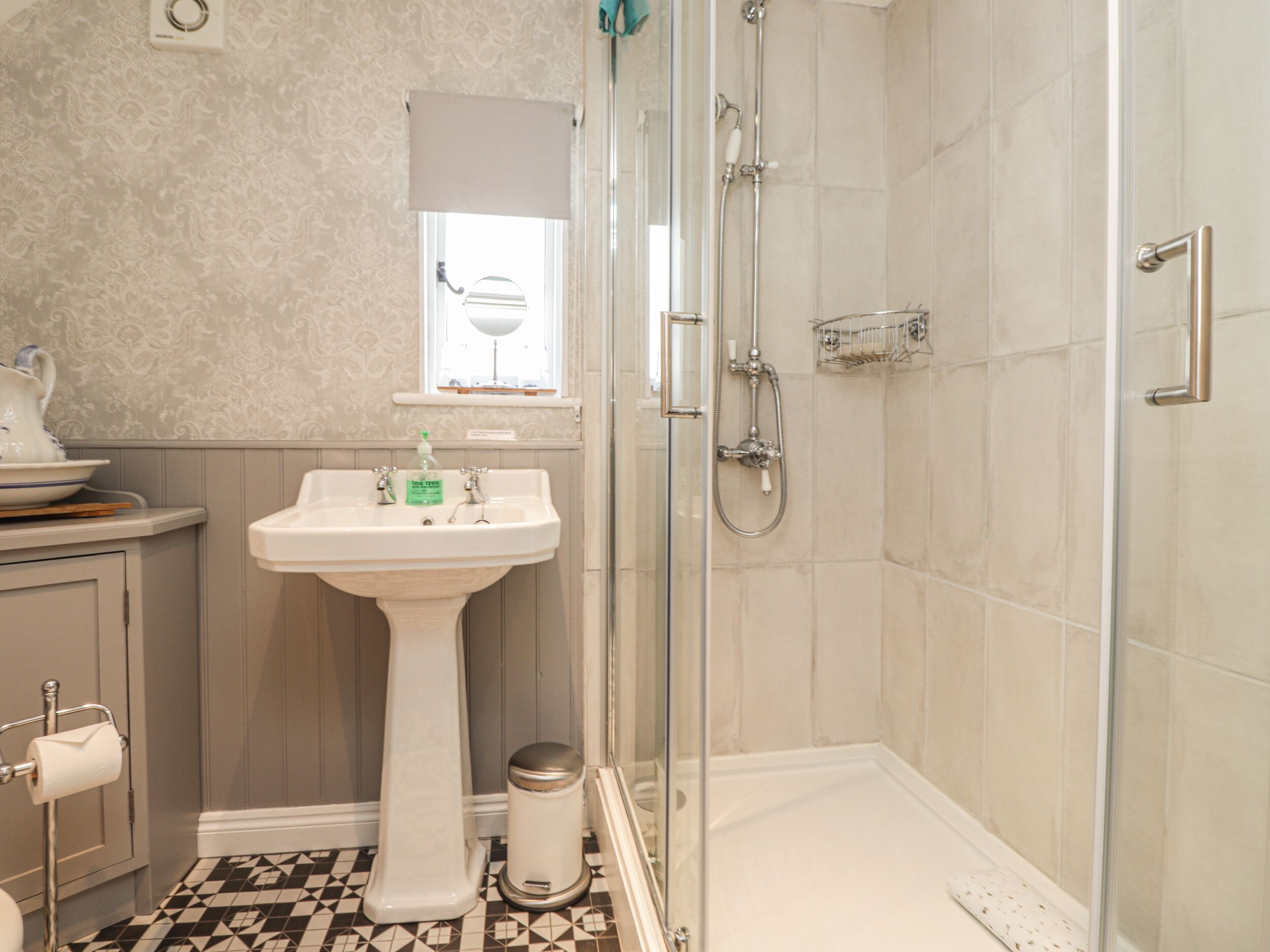 A bathroom with a pedestal sink, a glass shower enclosure, and a patterned floor.