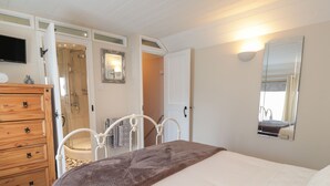 Un dormitorio con cama, cómoda de madera, espejo y zona de ducha.