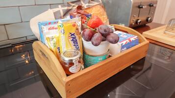 A wooden tray with breakfast items including bread, fruit, cereal, and spreads on a kitchen counter.