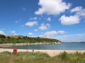 A beach with a clear sky, calm sea, and grassy hills in the background. - Chyandour (Falmouth)