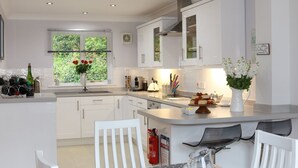 A modern kitchen with white cabinetry, a dining area with a table and chairs, and a window with a view of greenery. - Chyandour (Falmouth)