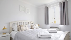 A neatly arranged bedroom with a bed, bedside tables, and a window with curtains. - Chyandour (Falmouth)