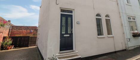 A two-story building with a black front door, a small window with a number '25' above it, and a brick wall adjacent to it.