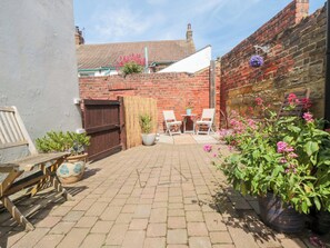 A brick patio with a table and chairs, a wooden bench, and potted plants. - Sands End Cottage (Redcar)