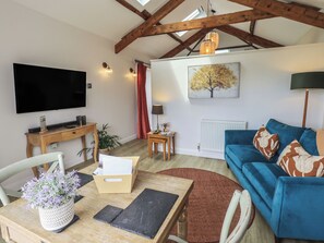 A living room with a flat-screen TV, a blue sofa, a wooden dining table, and a red patterned rug. - Acorn (Ambleside)