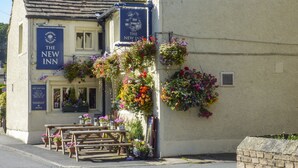 En traditionell pub som heter ”The New Inn”, med en fasad av sten, träbänkar utomhus och hängande blomkorgar.