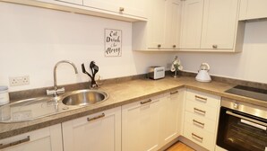 A modern kitchen with white cabinets, a stainless steel sink, a toaster, and a kettle. - Foxes Den (Thornton-Cleveleys)