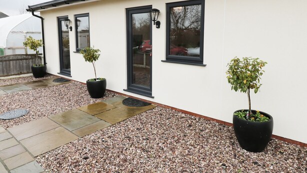 A white building with black-framed windows and doors, a gravel pathway, and potted plants. - Foxes Den (Thornton-Cleveleys)