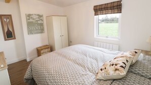 A bedroom with a bed, a wardrobe, a window with a view of a green field, and a chandelier. - Foxes Den (Thornton-Cleveleys)