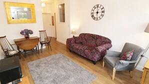 A living room with a sofa, chairs, a coffee table, a rug, a clock, and a television. - Foxes Den (Thornton-Cleveleys)