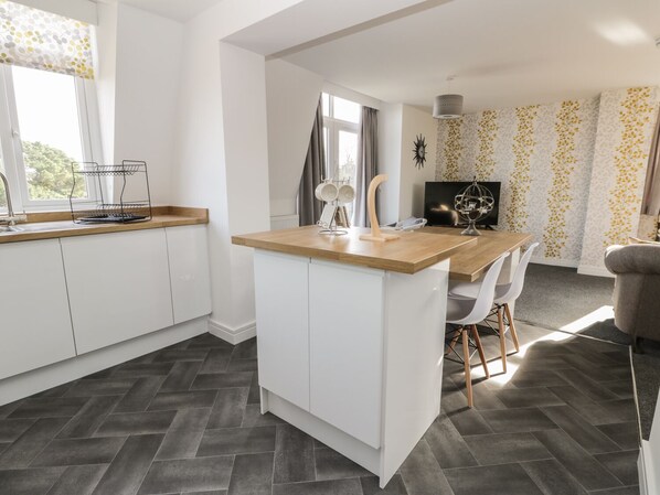 A modern kitchen with white cabinets, a wooden countertop, and a herringbone-patterned floor.