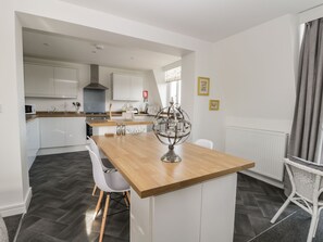 A modern kitchen with white cabinets, a wooden countertop, and a dining area with a white chair and a globe decoration.
