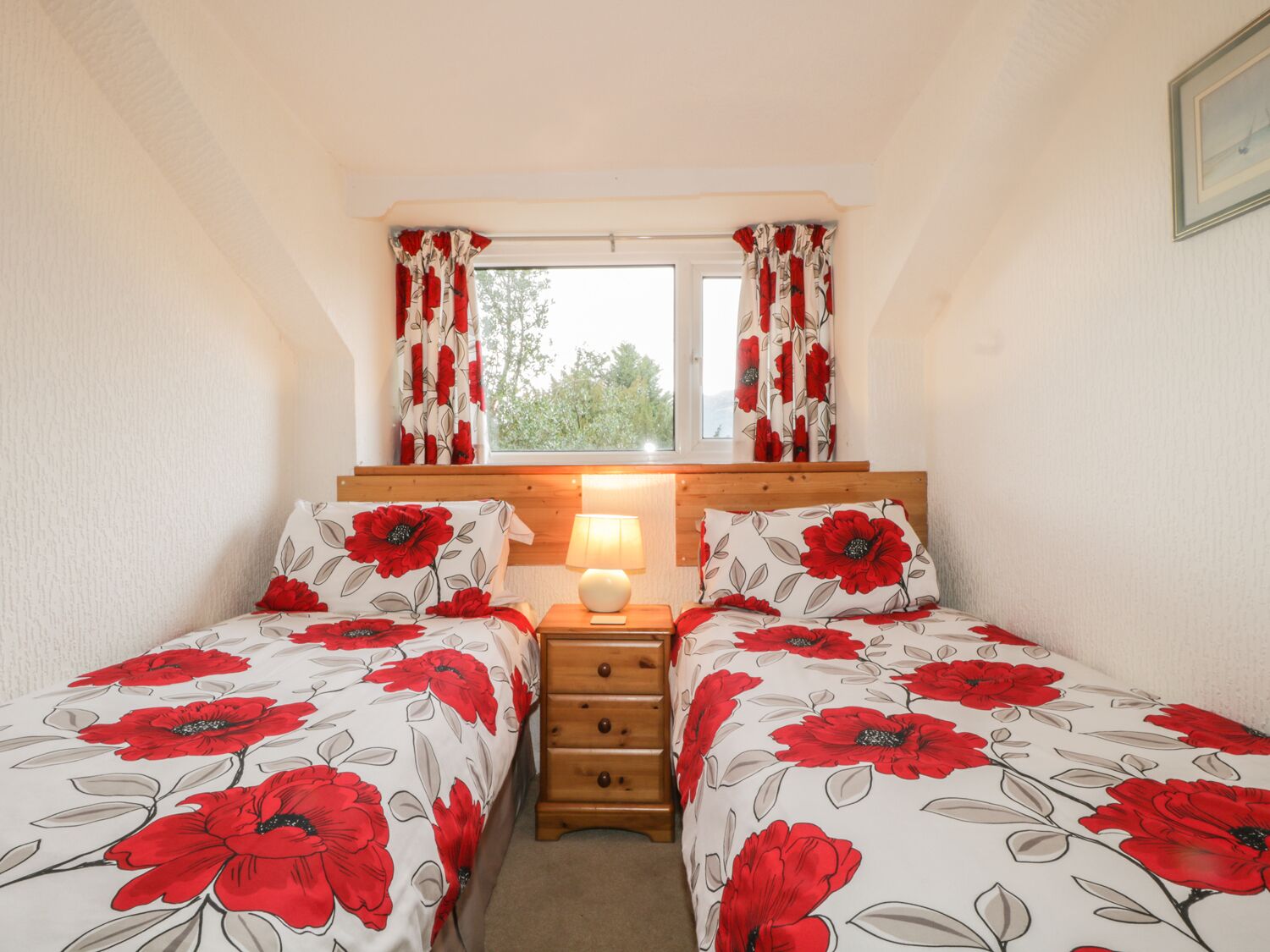 A bedroom with two beds, a window with curtains, a bedside lamp, and a wooden headboard.