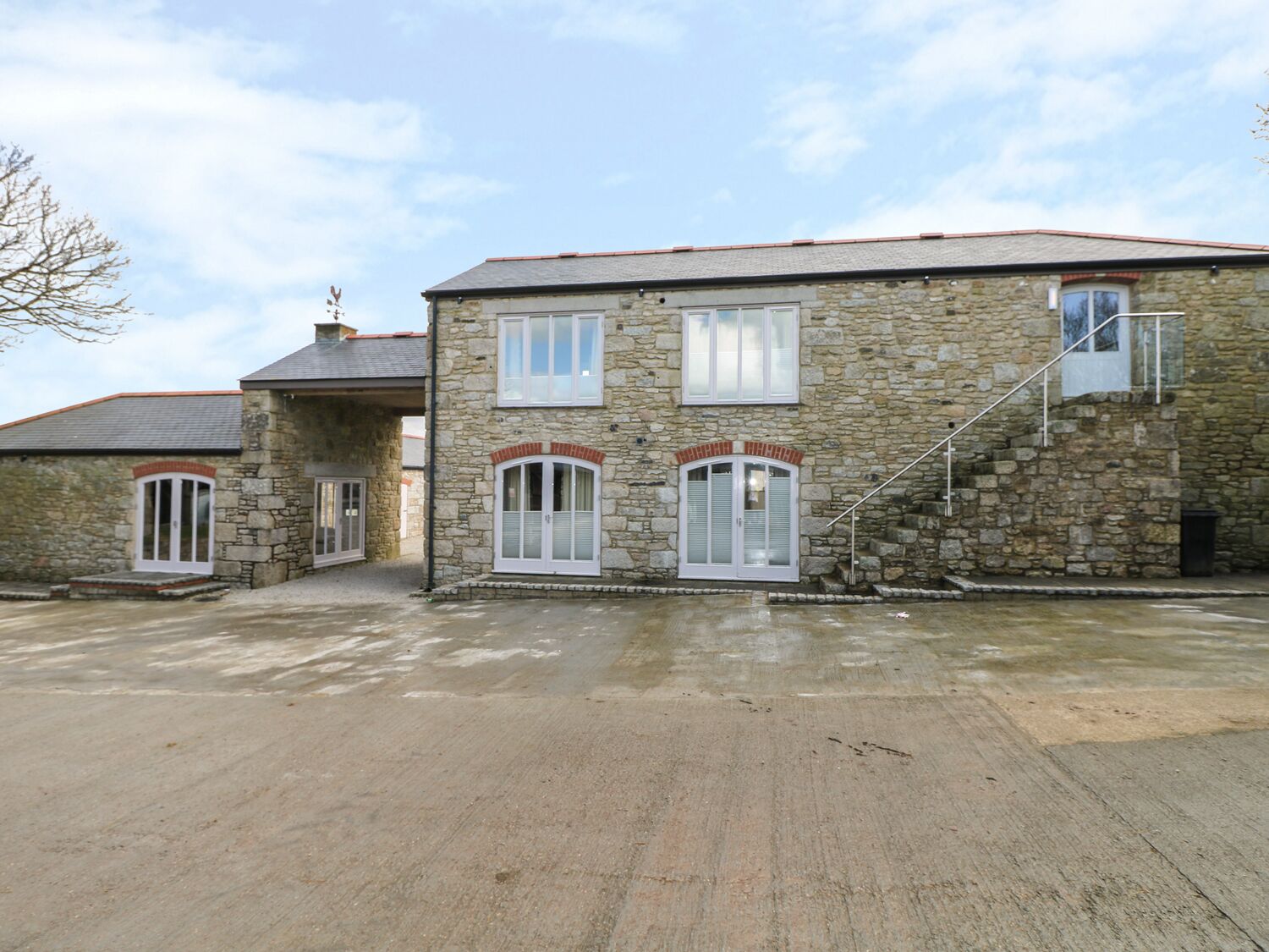 A stone building with a staircase leading to the upper floor, a covered entrance, and a paved driveway.