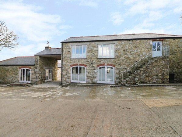 A stone building with a staircase leading to the upper floor, a covered entrance, and a paved driveway. - Argal (Penryn)