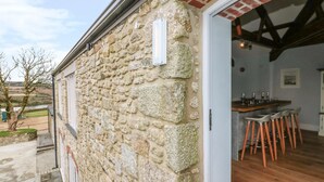 Pared exterior de piedra con una puerta de madera que da a un espacio interior con una zona de bar y taburetes.