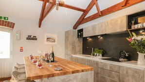 Una cocina moderna con una isla de madera, armarios grises y una salpicadura trasera negra. Hay taburetes de bar, un fregadero y una tetera en la encimera.