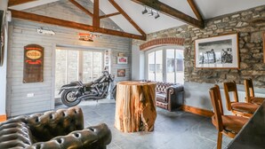 Un interior espacioso con vigas de madera a la vista, una pared de piedra, una motocicleta, muebles de cuero y un cuadro enmarcado.
