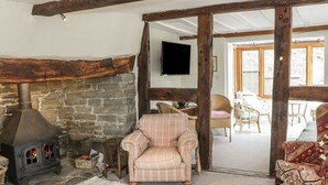 Un salón acogedor con chimenea de piedra, un sillón a cuadros y muebles de mimbre.